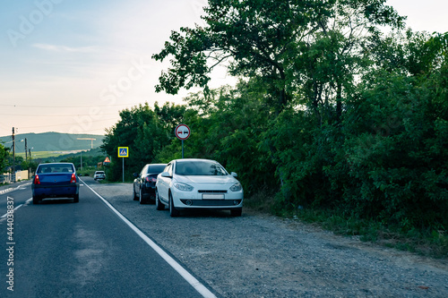Parked cars on the sidelines on a country road. Cars on the edge of a road in the countryside during the day. © Ilya_R