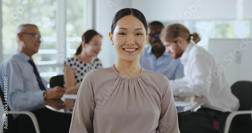 Medium shot of asian businesswoman looking at camera sitting at table with colleagues in boardroom