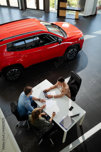 Female car seller sitting in car salon with a customers and discussing about car performances.