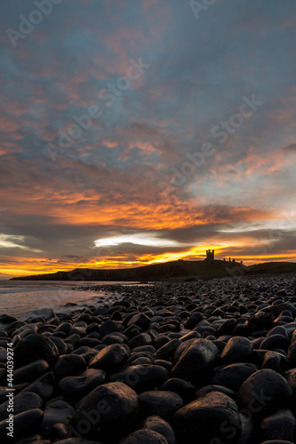 The most beautiful sunrise at Dunstanburgh Castle with the famous slippery black boulders in Northumberland, as the sky erupted with colour