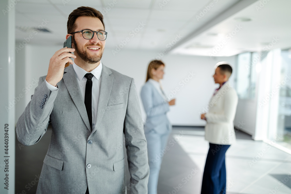photo of young smiling businessman having phone call while standing in hallway before meeting. photo of young smiling businessman having phone call while standing in hallway before meeting.