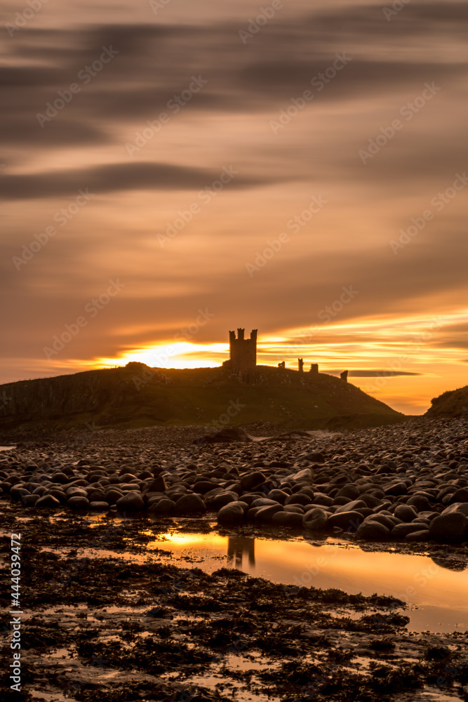 The most beautiful sunrise at Dunstanburgh Castle with the famous slippery black boulders in Northumberland, as the sky erupted with colour