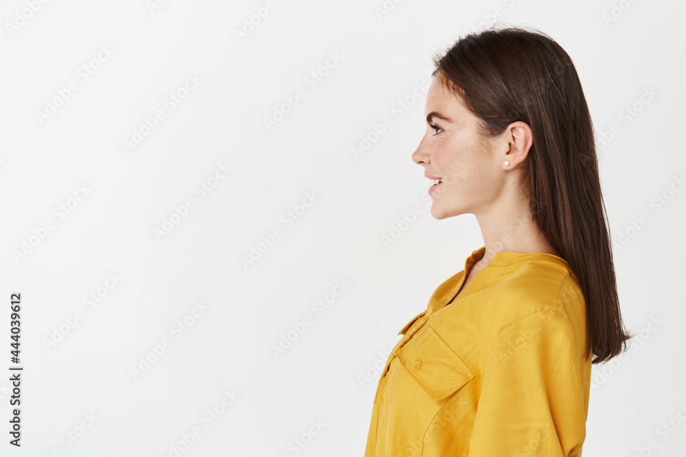 Profile portrait of young confident woman standing on white background, looking left and smiling, wearing yellow blouse Profile portrait of young confident woman standing on white background, looking left and smiling, wearing yellow blouse