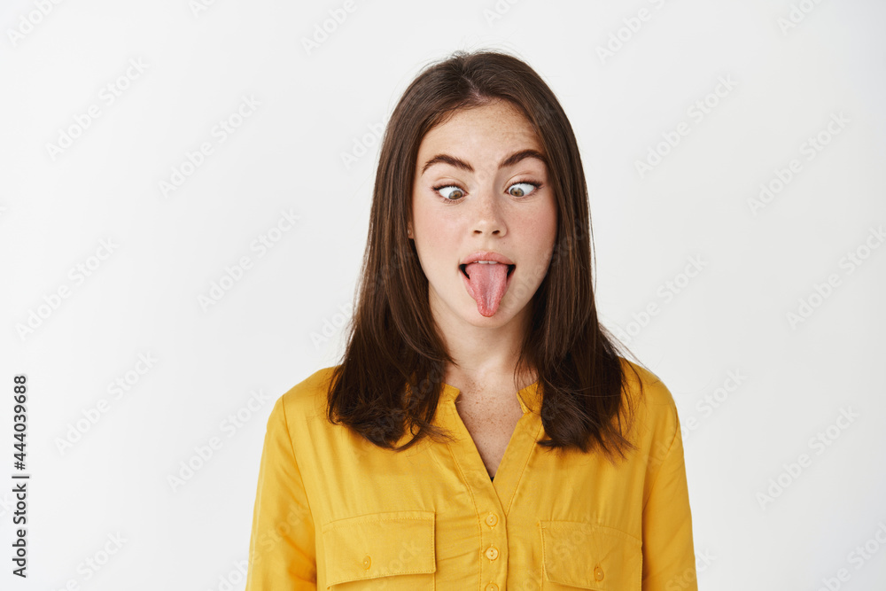Funny and playful young woman making faces, squinting eyes and showing tongue, standing over white background Funny and playful young woman making faces, squinting eyes and showing tongue, standing over white background