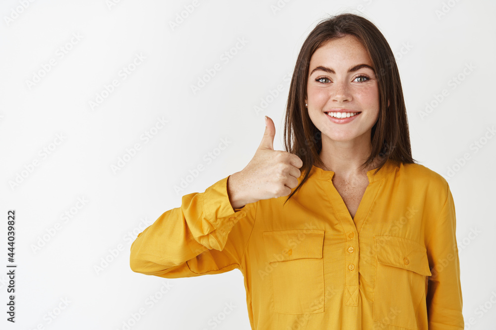 Beautiful young woman showing thumb-up and smiling, nod in approval, agree and like your choice, recommending product, standing over white background Beautiful young woman showing thumb-up and smiling, nod in approval, agree and like your choice, recommending product, standing over white background