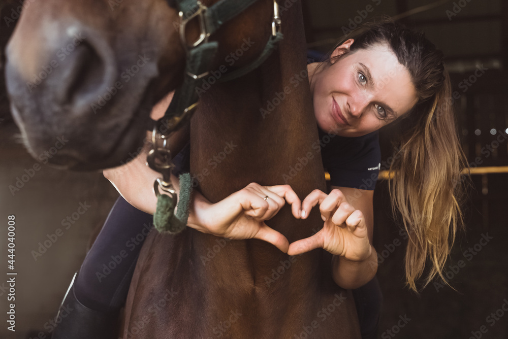 Horsewoman posing with her seal brown horse in the stable. Girl making