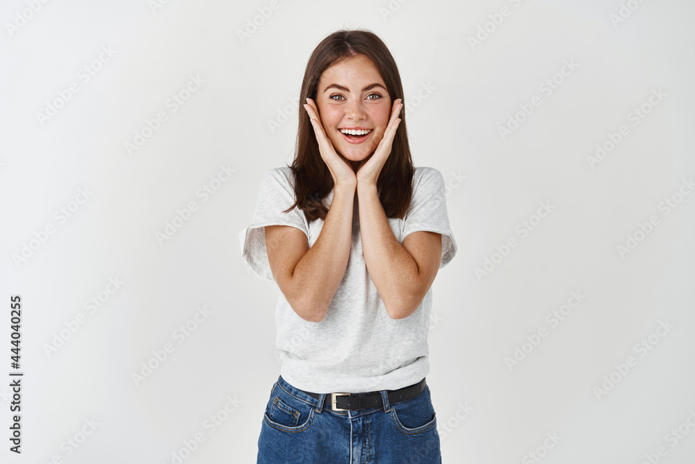 Beauty. Surprised lovely woman touching face and smiling excited, standing over white background Beauty. Surprised lovely woman touching face and smiling excited, standing over white background