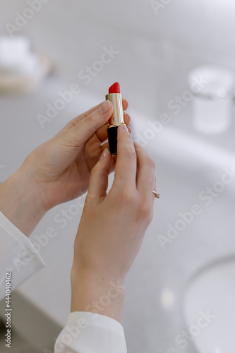 Red lipstick in female hands woman is making up in the bathroom for a holiday