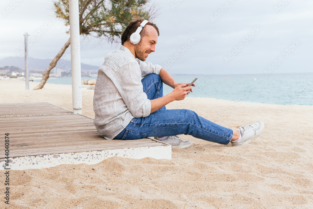 Happy man in headphones using smartphone on beach Happy man in headphones using smartphone on beach