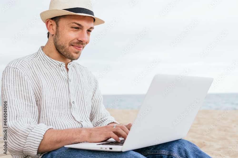 Trendy man using laptop on beach Trendy man using laptop on beach