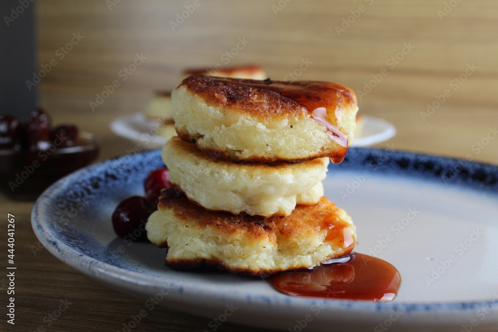 Three pancake cheesecakes lie stack of slides on top of each other on plate table with cherry cherry . View from the side. Breakfast is Russian Ukrainian. Dishes cottage cheese. Place with copyspace Three pancake cheesecakes lie stack of slides on top of each other on plate table with cherry cherry . View from the side. Breakfast is Russian Ukrainian. Dishes cottage cheese. Place with copyspace