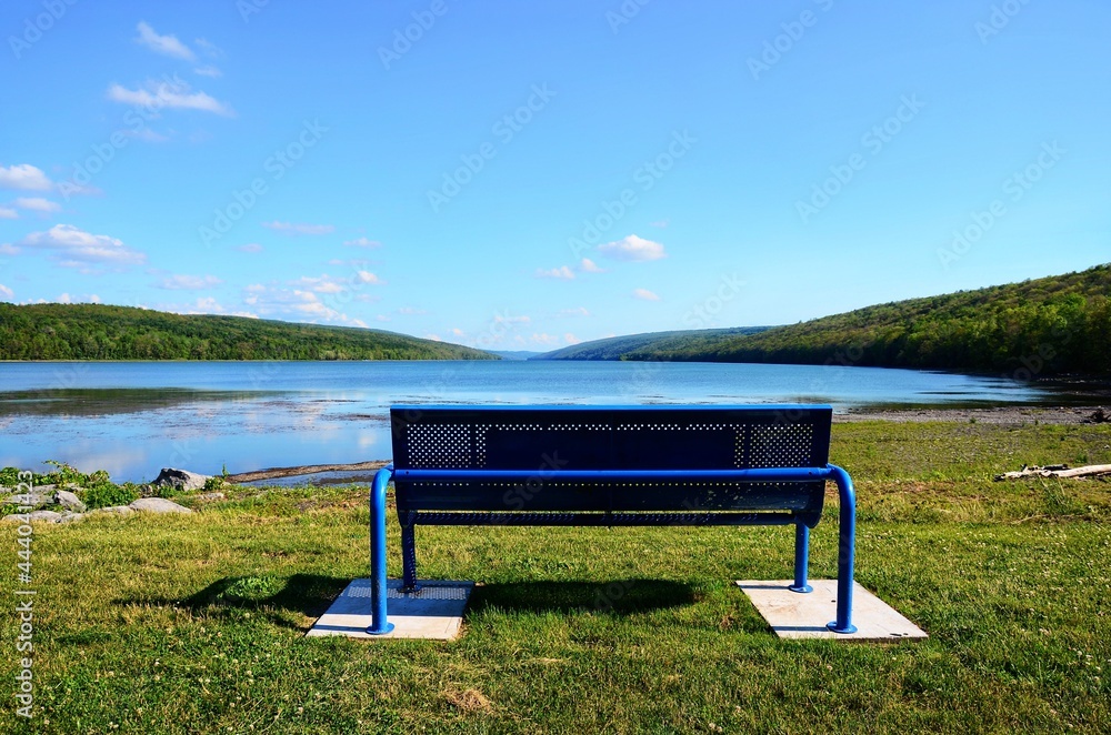 Obraz premium Bench on the lake. Overlooking Hemlock Lake, one of the minor Finger Lakes, located in Livingston County, New York, south of Rochester. It’s forever-wild, tranquil landscape. 