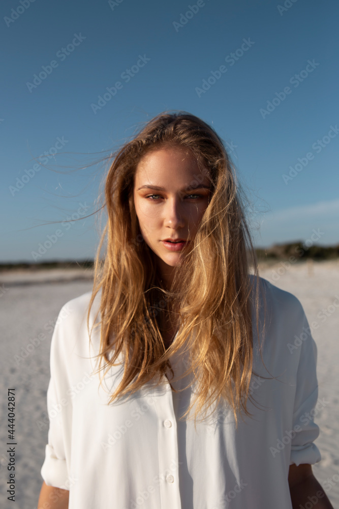 Blonde woman with long hair standing on the beach looking at camera Blonde woman with long hair standing on the beach looking at camera