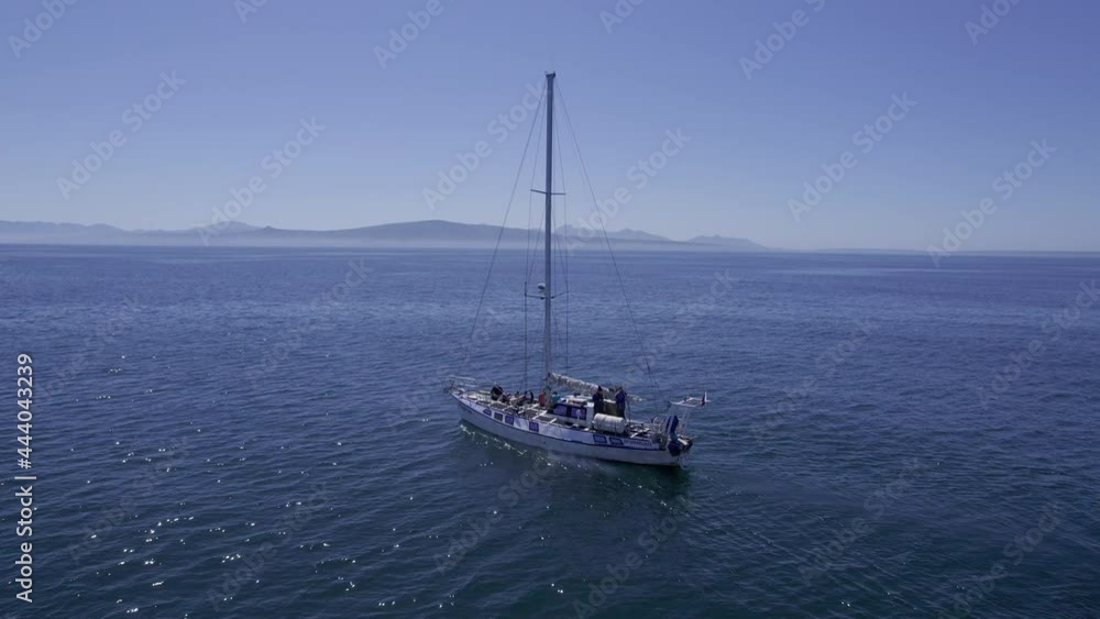 Circling shot from drone of yacht in a middle of oceanic landscape. Small boat with crew and mountains on background. Ship in still waters of Pacific ocean on bright day. Concept of travel, adventure. Circling shot from drone of yacht in a middle of oceanic landscape. Small boat with crew and mountains on background. Ship in still waters of Pacific ocean on bright day. Concept of travel, adventure.
