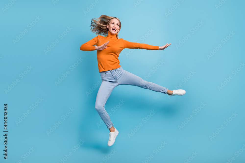 Photo of adorable strong young lady wear orange sweater jumping high practicing karate smiling isolated blue color background