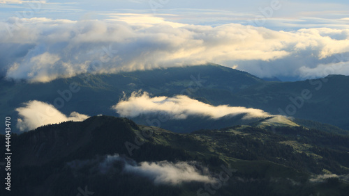View from Mount Brienzer Rothorn, Switzerland. Summer morning after a lot of rainfall. Bright lit clouds and fog lifting over green hills in Entlebuch, Lucerne Canton.