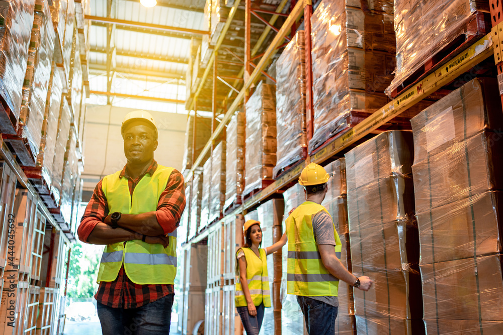 Portrait of black male worker team working in factory warehouse. Black man worker smiling with crossed arms indoor of building in background shelves with goods.Logistic industry concept.