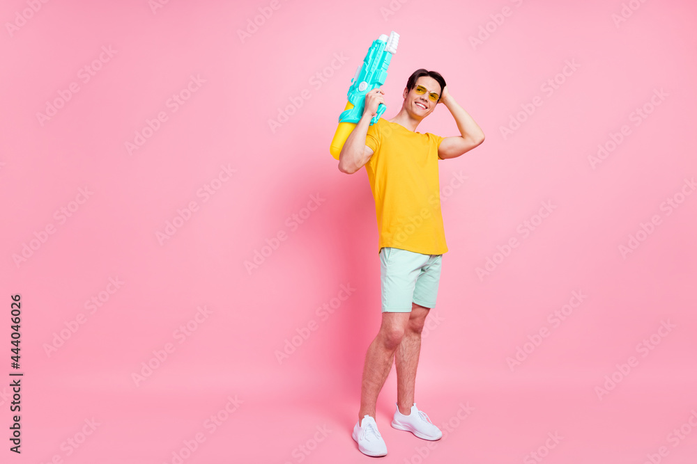 Full size photo of young guy happy positive smile hold water pistol squirt hand touch hair isolated over pastel color background Full size photo of young guy happy positive smile hold water pistol squirt hand touch hair isolated over pastel color background