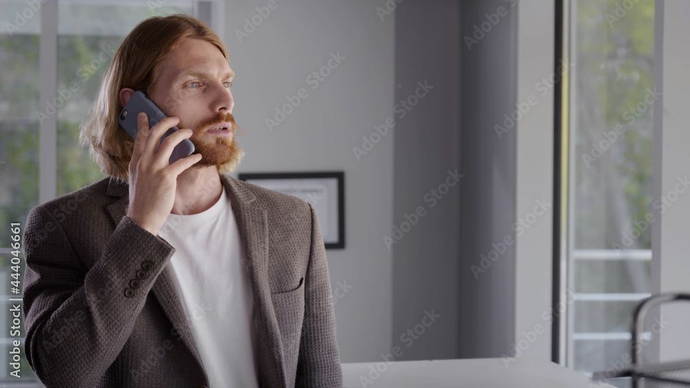 Businessman calling by smartphone while standing by office window Businessman calling by smartphone while standing by office window