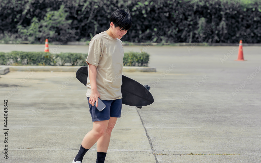 Portrait adult sportive Asian skater wearing hipster shirt with shorts, smiling with happiness, holding skateboard and standing outdoor with copy space. Activity and Adventure Concept.