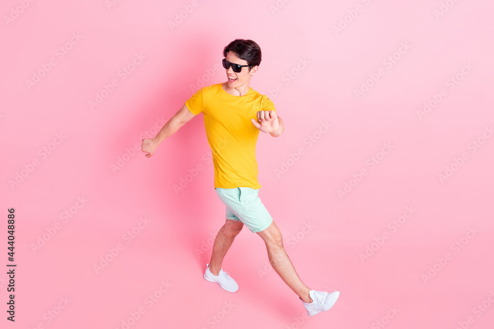 Photo of funky pretty young man wear yellow t-shirt dark eyewear smiling walking dancing isolated pink color background