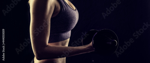 Slim athletic woman Holding dumbbell in the hand on black photo