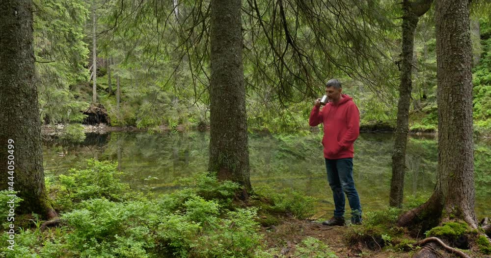 Bearded man drinks tea from a mug near a mountain lake Bearded man drinks tea from a mug near a mountain lake