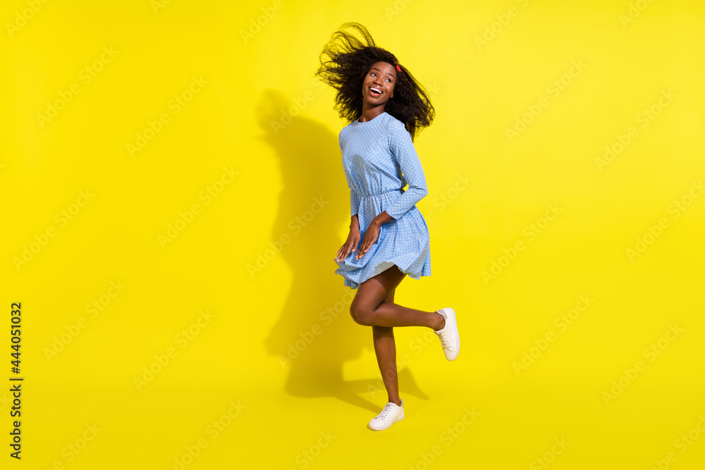 Full length body size photo of dancing girl in blue dotted dress looking empty space isolated on bright yellow color background