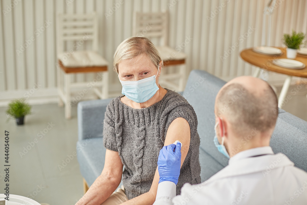 Man doctor vaccinates an elderly woman at her home wearing a protective mask. Vaccination concept Man doctor vaccinates an elderly woman at her home wearing a protective mask. Vaccination concept