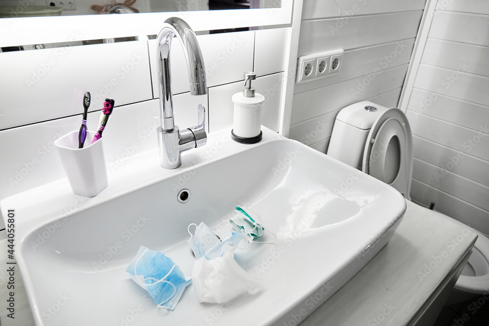 Fototapeta premium Used medical masks lie in the sink waiting a washing. White color bathroom. Disinfecting and saving money to be used again. Reusable. Family health care and save the budget concept. Epidemic hygiene