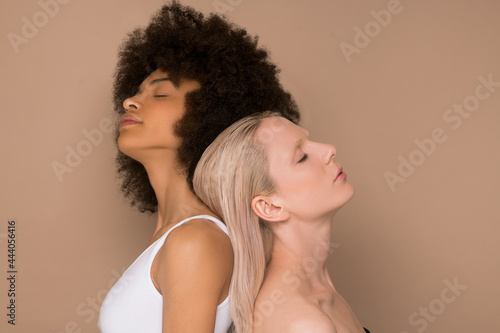 A dark-haired woman and a blonde woman standing back to back photo