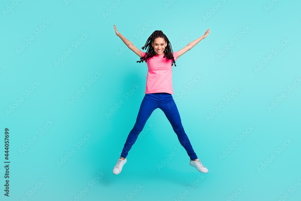 Photo of positive funny girl jump have fun raise hands wear pink t-shirt isolated on blue color background