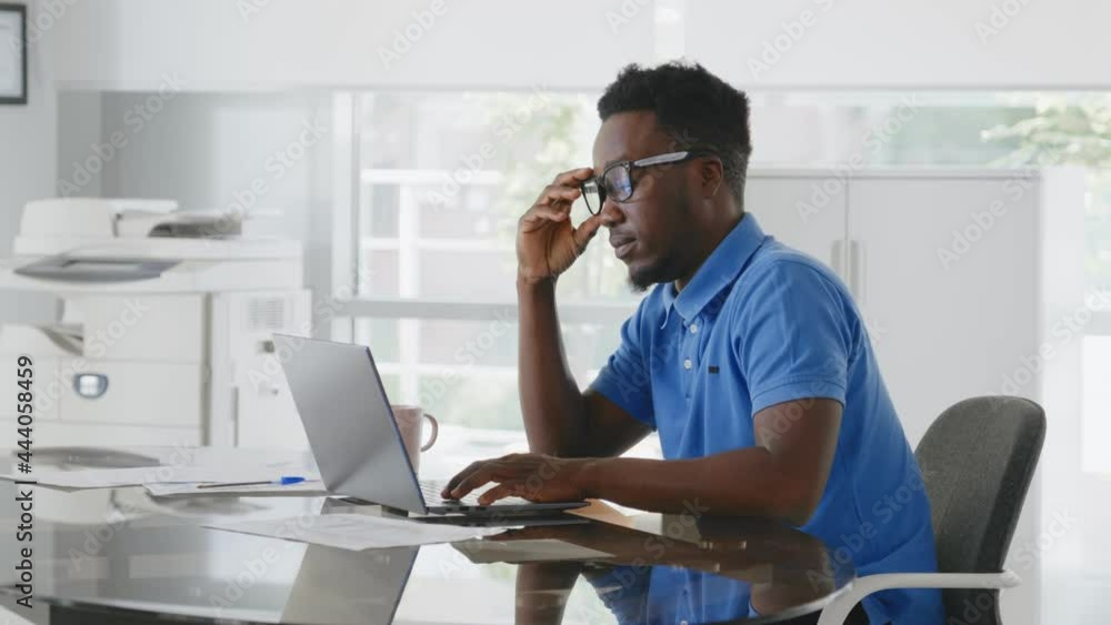 Tired young businessman overworking sitting at desk with laptop in modern office Tired young businessman overworking sitting at desk with laptop in modern office
