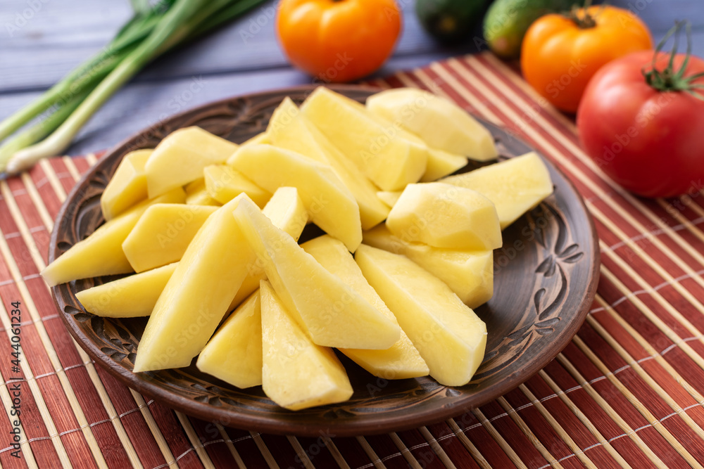 Tubers of raw peeled cut potatoes on a plate on the kitchen table with vegetables. Preparation for cooking. Tubers of raw peeled cut potatoes on a plate on the kitchen table with vegetables. Preparation for cooking.