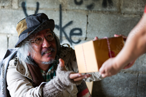 Homeless man receiving gift box from people hands at abandoned building or on street in the city