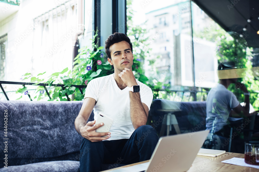 Thoughtful male freelancer with modern laptop and cellular device pondering on ideas for release text for sharing at web page, pensive man with digital technology thinking about remote working Thoughtful male freelancer with modern laptop and cellular device pondering on ideas for release text for sharing at web page, pensive man with digital technology thinking about remote working