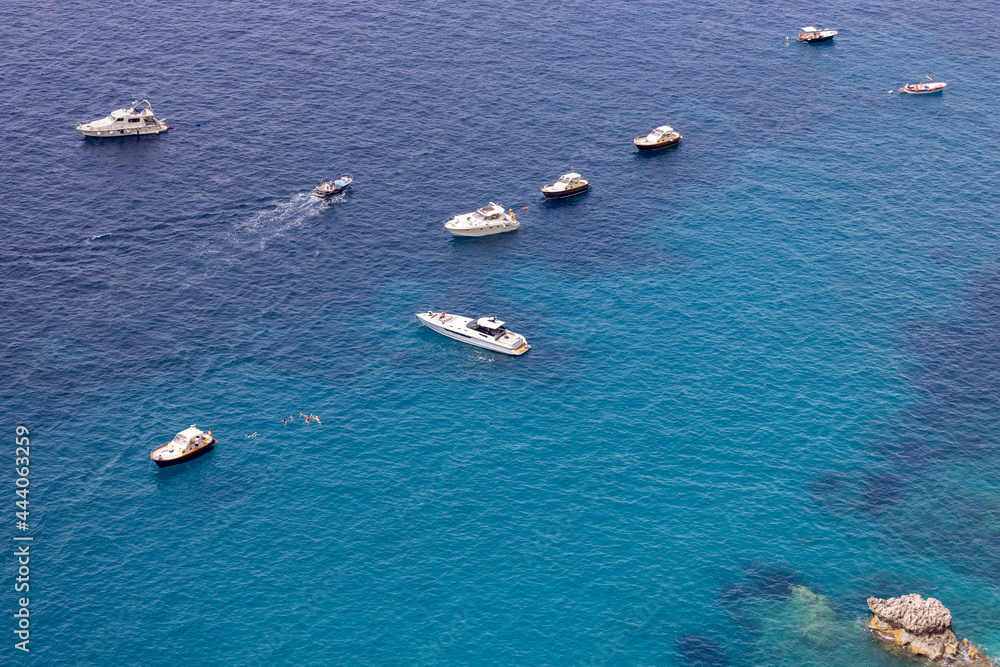 Aerial view of rocky shoreline on the Tyrrhenian Sea nearby Marina Piccola, a lot of sailing tourist boats, Capri Island, Italy