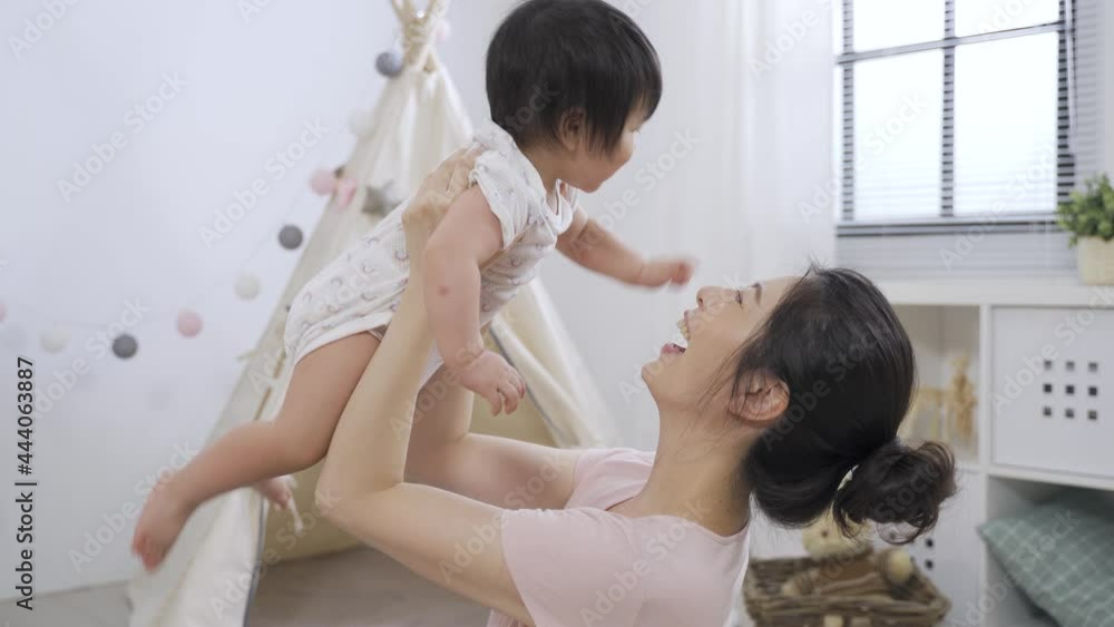 portrait asian loving mother is playing with her lovely baby daughter by lifting her up and smiling at her with happiness in cute child’s game room. portrait asian loving mother is playing with her lovely baby daughter by lifting her up and smiling at her with happiness in cute child’s game room.