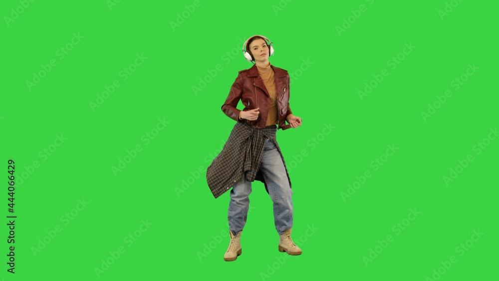 Young girl in stylish clothes starts to dance while listening to music with headphones on a Green Screen, Chroma Key. Young girl in stylish clothes starts to dance while listening to music with headphones on a Green Screen, Chroma Key.
