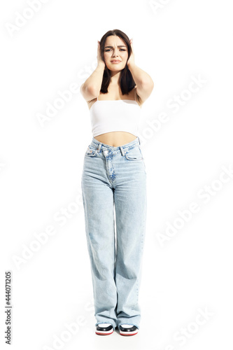Displeased young gen Z woman covering ears from loud conversation or music. Full body portrait isolated on white background