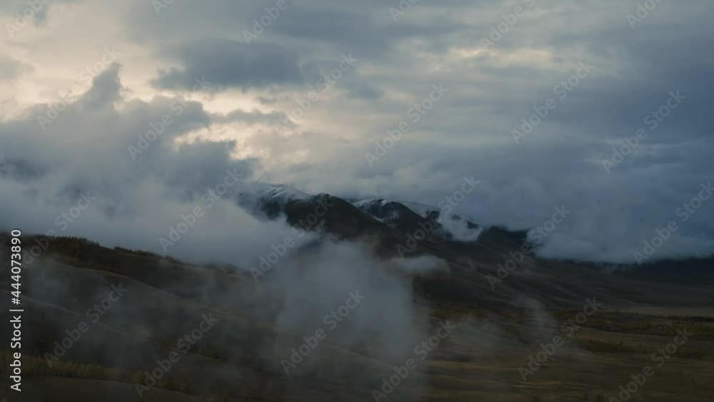 Clouds and fog over snowy mountain and valley ridge at sunset. Flying over peaks of Altai mountains on calm evening against sky in autumn weather Clouds and fog over snowy mountain and valley ridge at sunset. Flying over peaks of Altai mountains on calm evening against sky in autumn weather