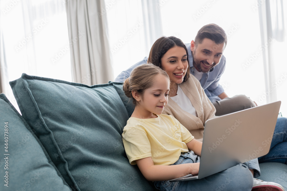 happy parents looking at daughter using laptop on couch at home happy parents looking at daughter using laptop on couch at home