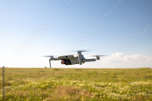 Flying white drone with digital camera in green field