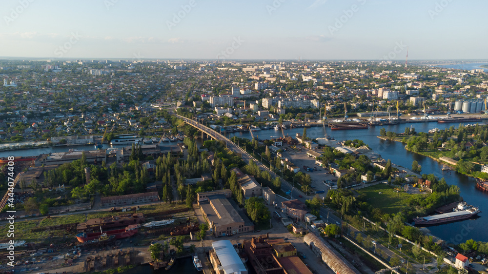 Aerial view of the Kherson city. A shipyard on the banks of the Dnieper River of which there are cranes and ships. Residential area with houses and greenery