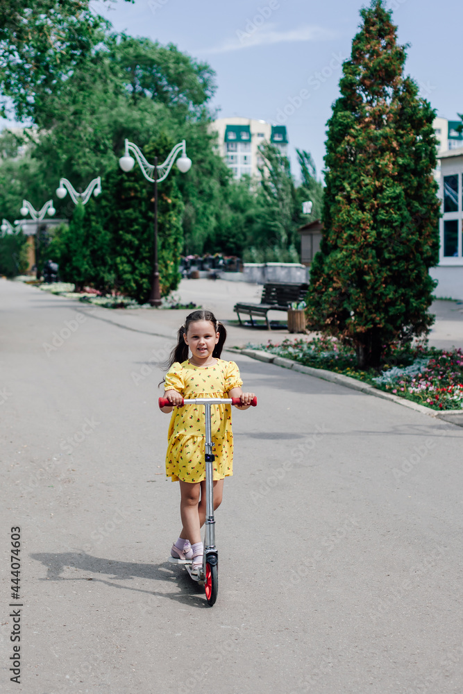 a cute girl in a yellow sundress learns to ride a scooter around the city and enjoys a hot summer day. 