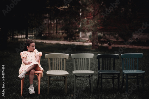 a lonely, sad girl in a dress sits on an empty row of chairs in the backyard of the outdoots and cries that no one came to her birthday.  photo