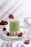 Strawberry matcha latte with strawberries on a white plate with beautiful shadows from the leaves.