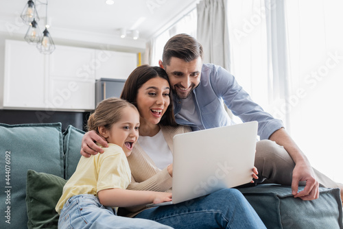 excited couple with daughter watching movie on laptop at home
