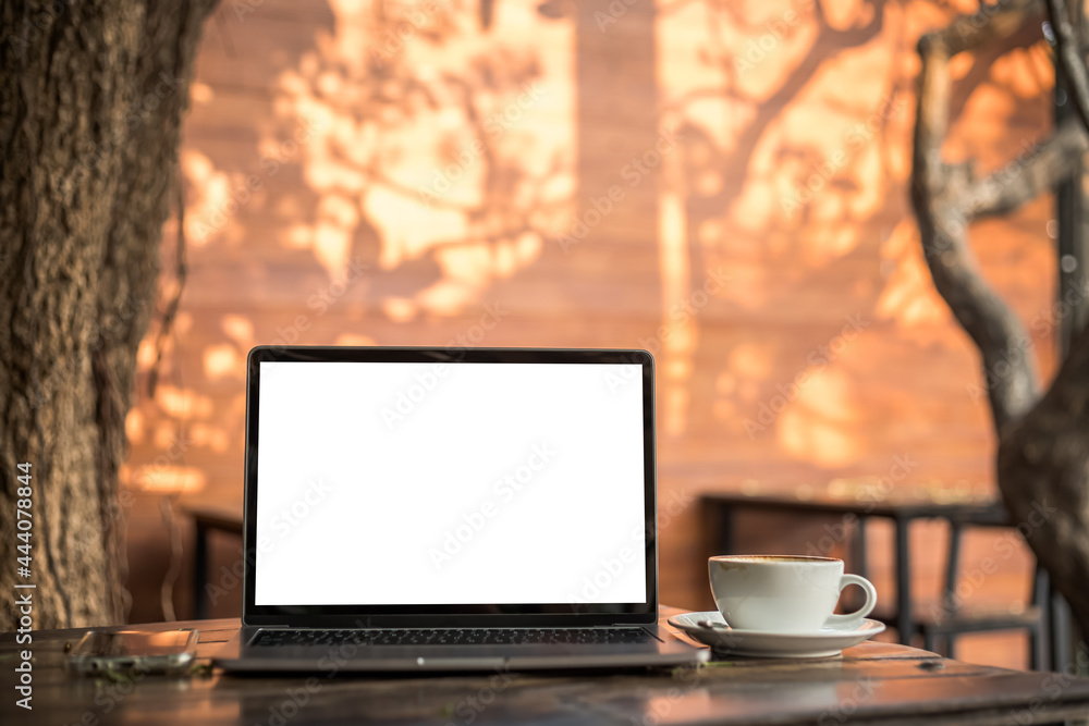 Fototapeta premium Mockup of laptop computer with empty screen with coffee cup and smartphone on table of tree branch shadow the cafe coffee shop background,White screen