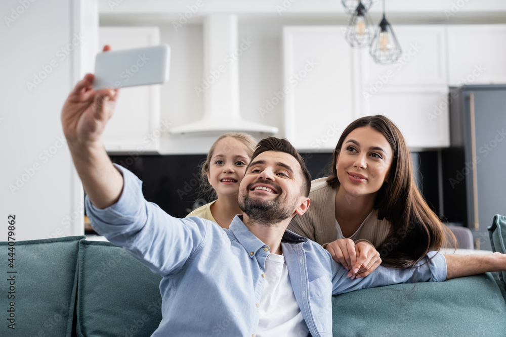cheerful man taking selfie on mobile phone with smiling family at home cheerful man taking selfie on mobile phone with smiling family at home